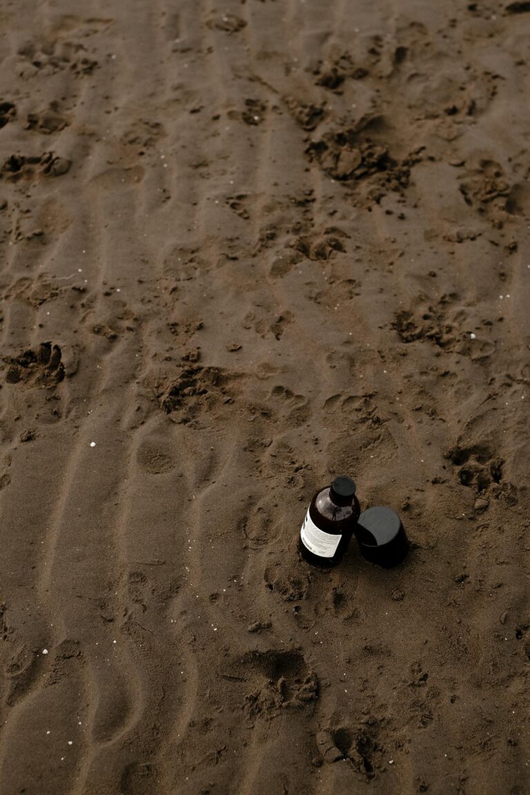 A natural cosmetic product bottle placed on a sandy beach surface.