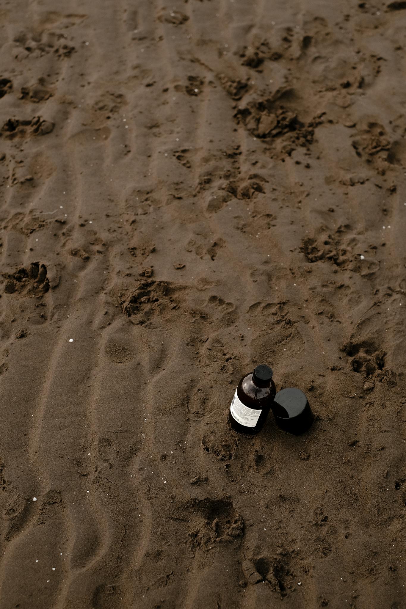A natural cosmetic product bottle placed on a sandy beach surface.