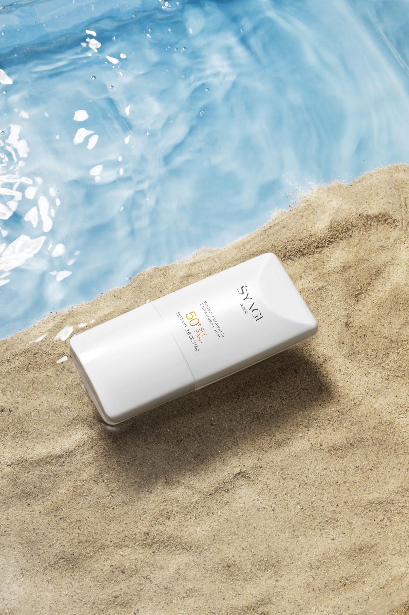 Close-up of a sunscreen bottle on sand beside clear blue water.